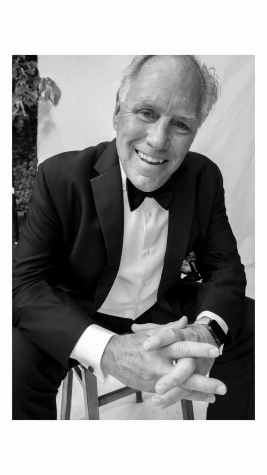 Guest in a tuxedo laughing, seated on the garden canvas set
